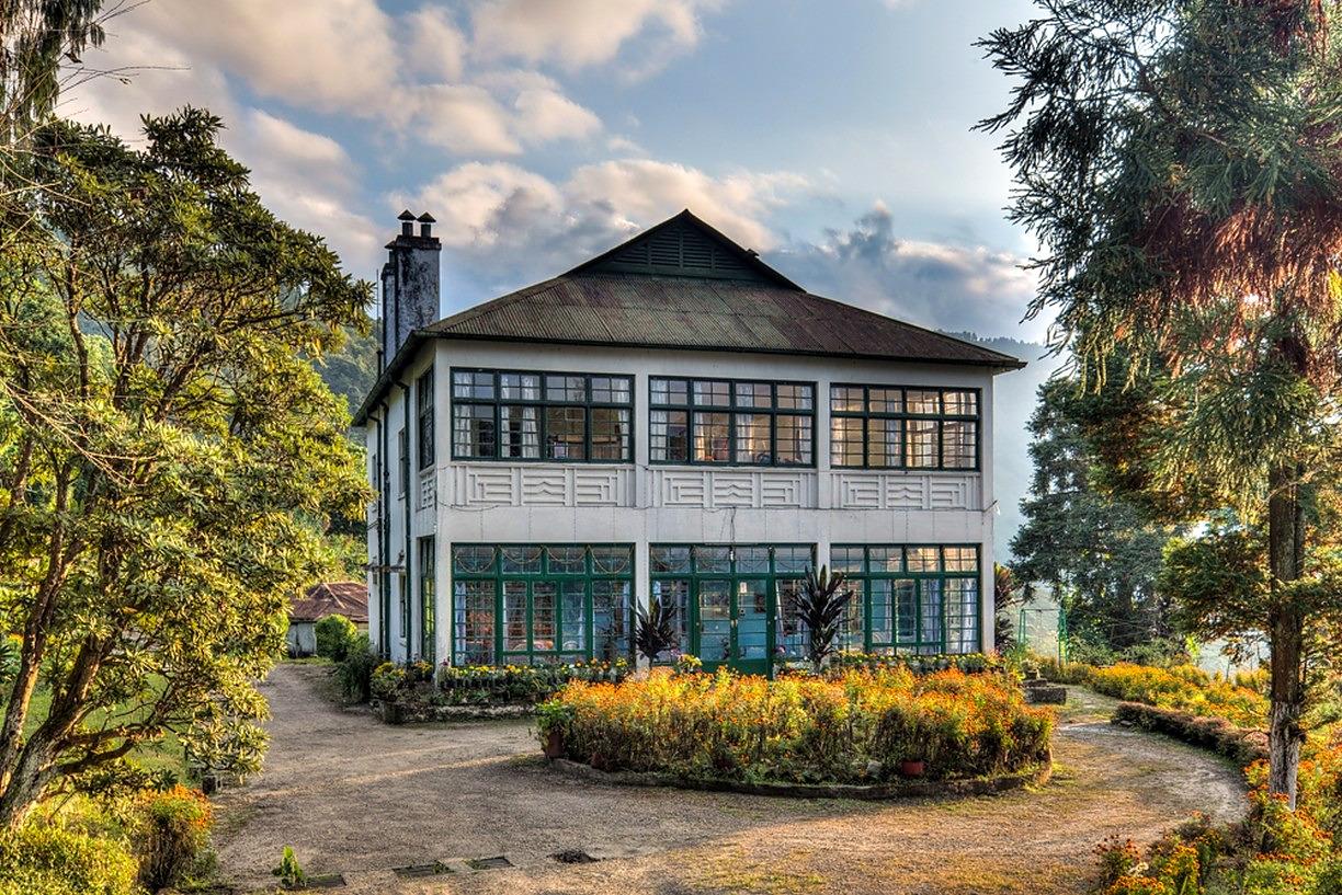 A white heritage bungalow with green-framed windows and a marigold garden